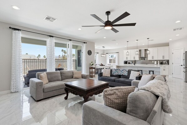 A spacious living room with a ceiling fan, a dining area, and a kitchen with white cabinets.