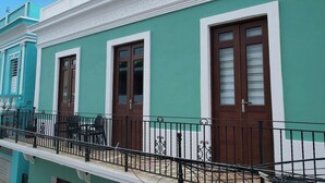 Un edificio con paredes exteriores azul turquesa y blancas, puertas grandes de color marrón y un balcón con barandilla metálica.