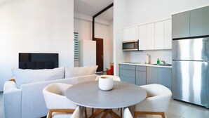 Una sala de estar moderna con un sofá gris, sillones blancos y una mesa redonda con un jarrón blanco. Un televisor de pantalla plana está montado en la pared.