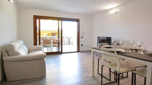 A modern living room with a sofa, a dining table set for four, and a sliding glass door leading to an outdoor area. - Amazing apartment in Olia Speciosa with WiFi (Olia Speciosa)