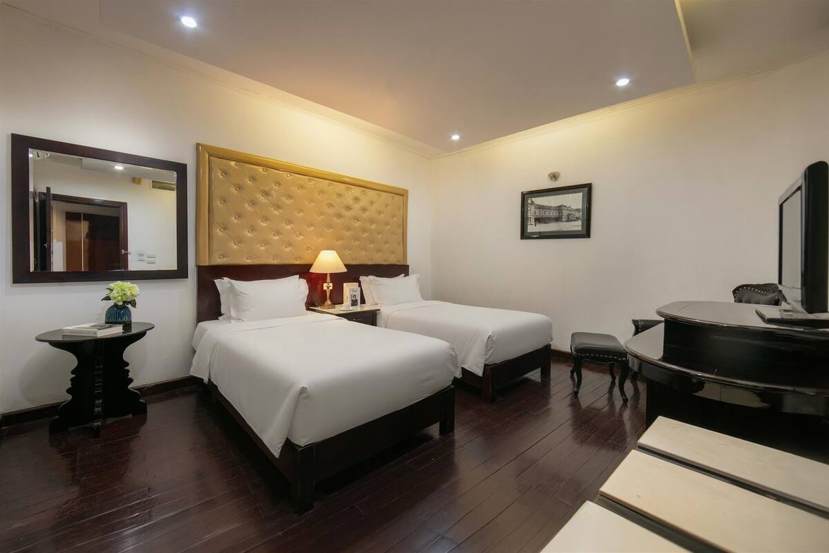 A hotel room with two beds, a desk, a chair, a vanity with a mirror, and a bathtub.