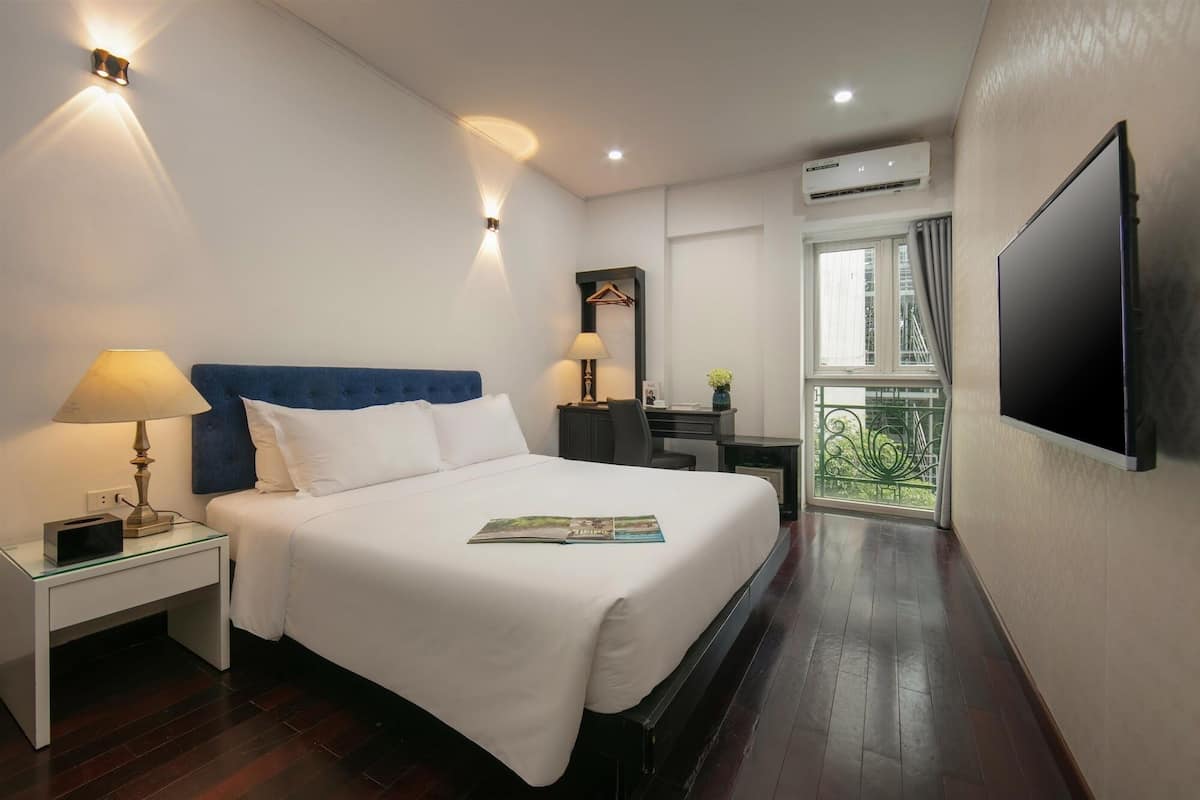 A hotel room with a bed, bedside table, lamp, desk, chair, and a TV mounted on the wall.