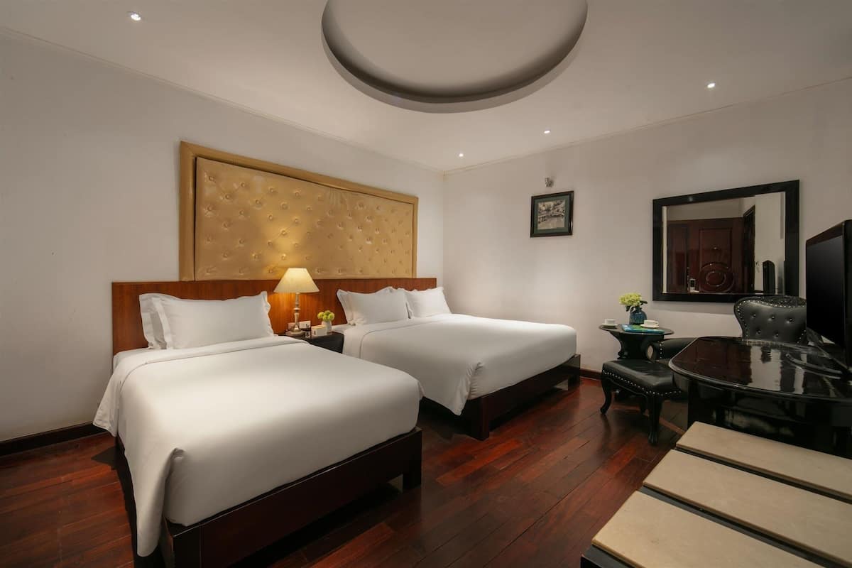 A hotel room with two beds, a desk, a chair, a TV, and a large painting on the wall.