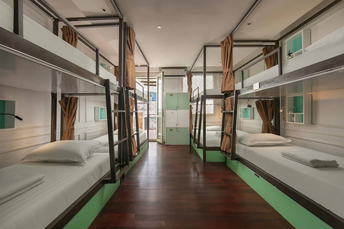 A corridor with bunk beds on both sides, a green wall, and a window with curtains.