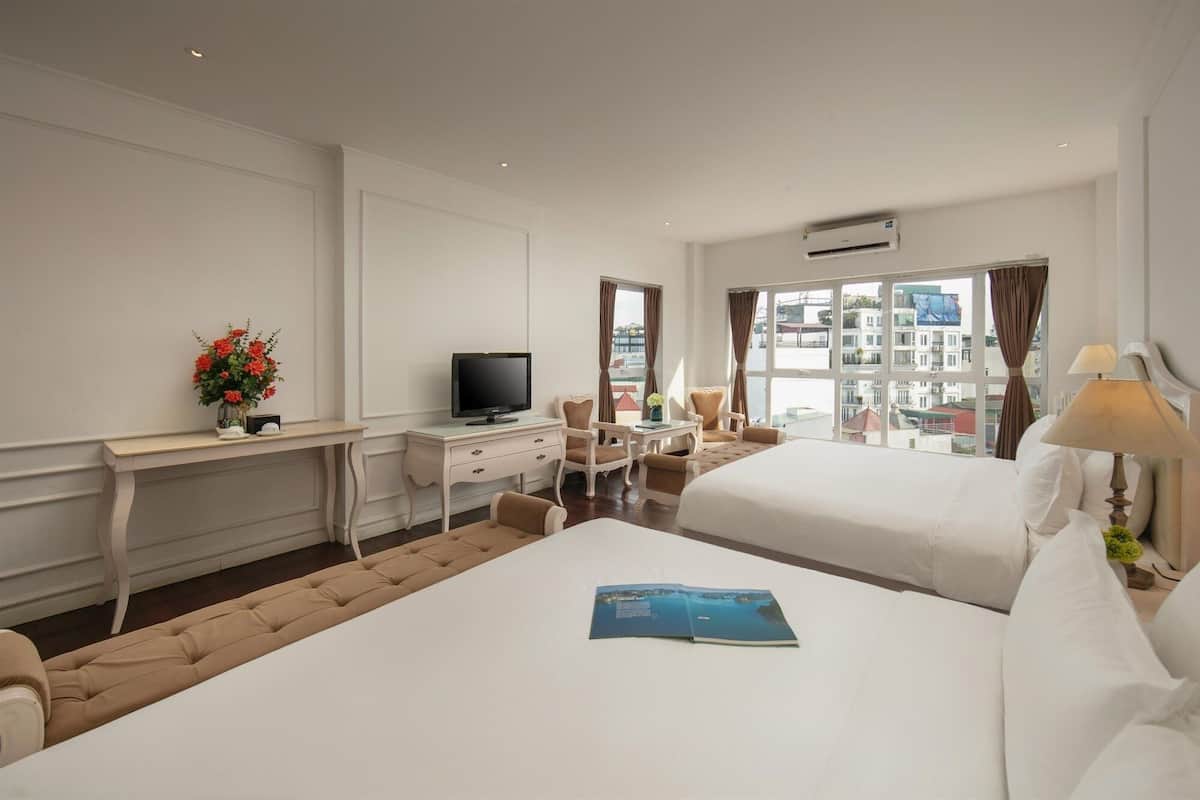A hotel room with a bed, a desk with a TV, a chair, and a view of the city.
