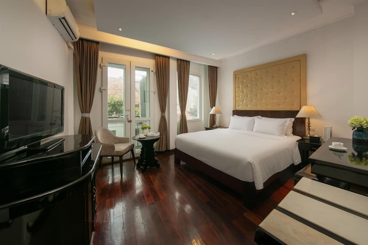 A hotel room with a large bed, a TV, a desk, and a chair.