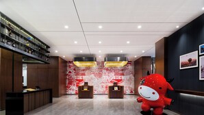 A reception area with a modern design, featuring a reception desk, two seating areas, and a large decorative wall. - UrCove By Hyatt Yangzhou Dongguan Street (Yangzhou)