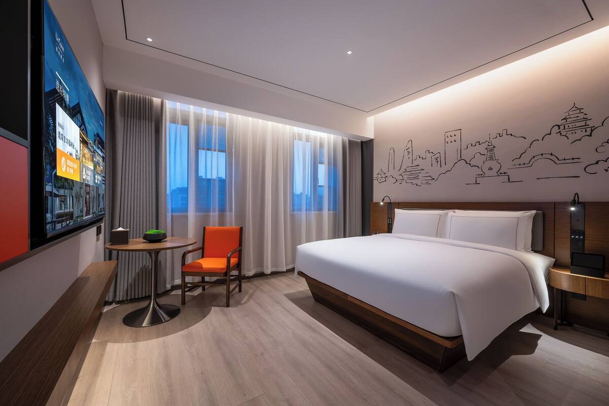 Una habitación de hotel moderna con una cama grande, un escritorio con una silla y un mural con vista a la ciudad en la pared.