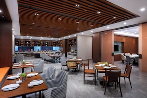 A modern restaurant with wooden ceiling panels, multiple dining areas, and a kitchen visible in the background. - UrCove By Hyatt Yangzhou Dongguan Street (Yangzhou)