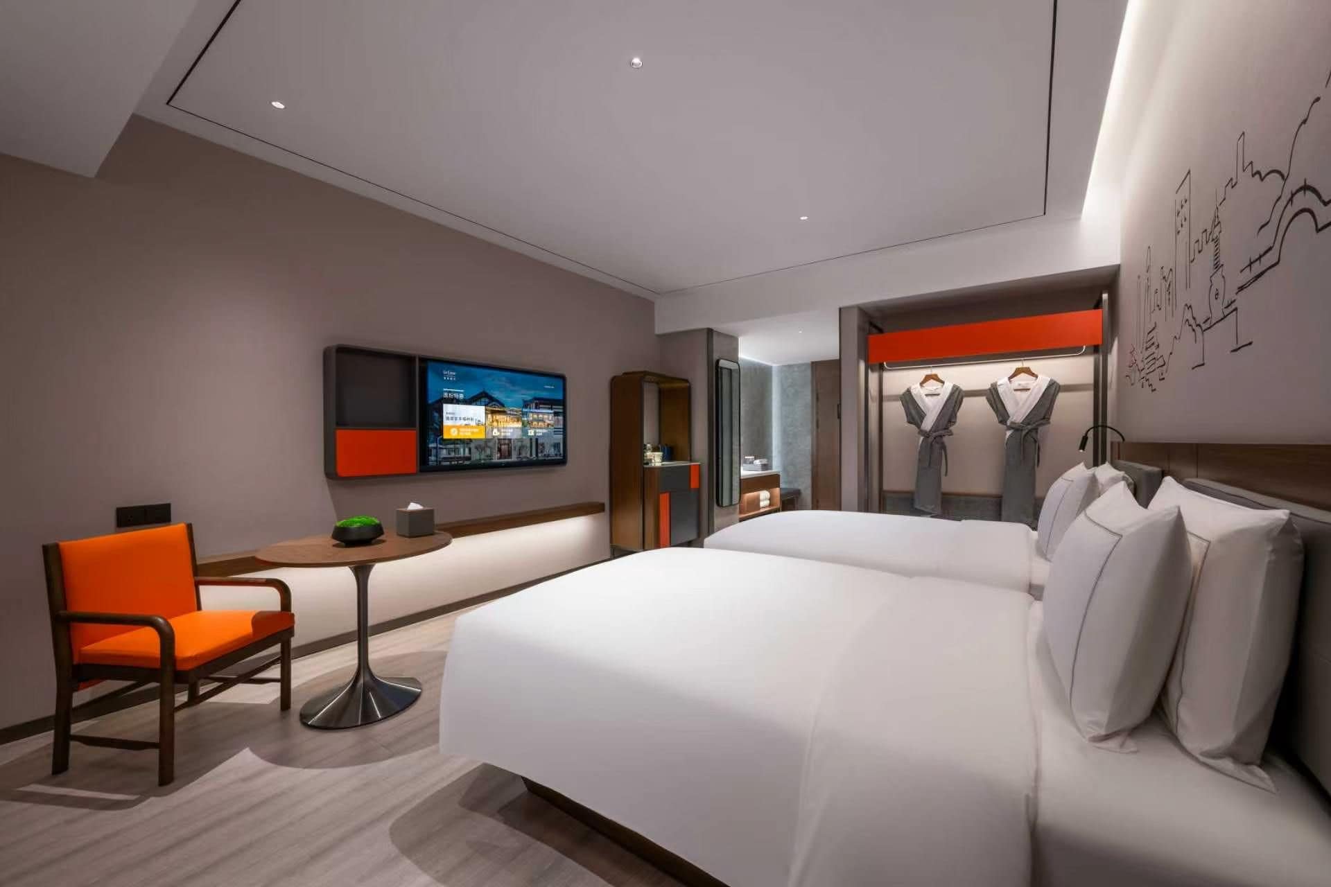 Ein modernes Hotelzimmer mit Bett, Schreibtisch, Stuhl, Fernseher und einem durchgehenden Tür sichtbar erkennbaren Badezimmer.