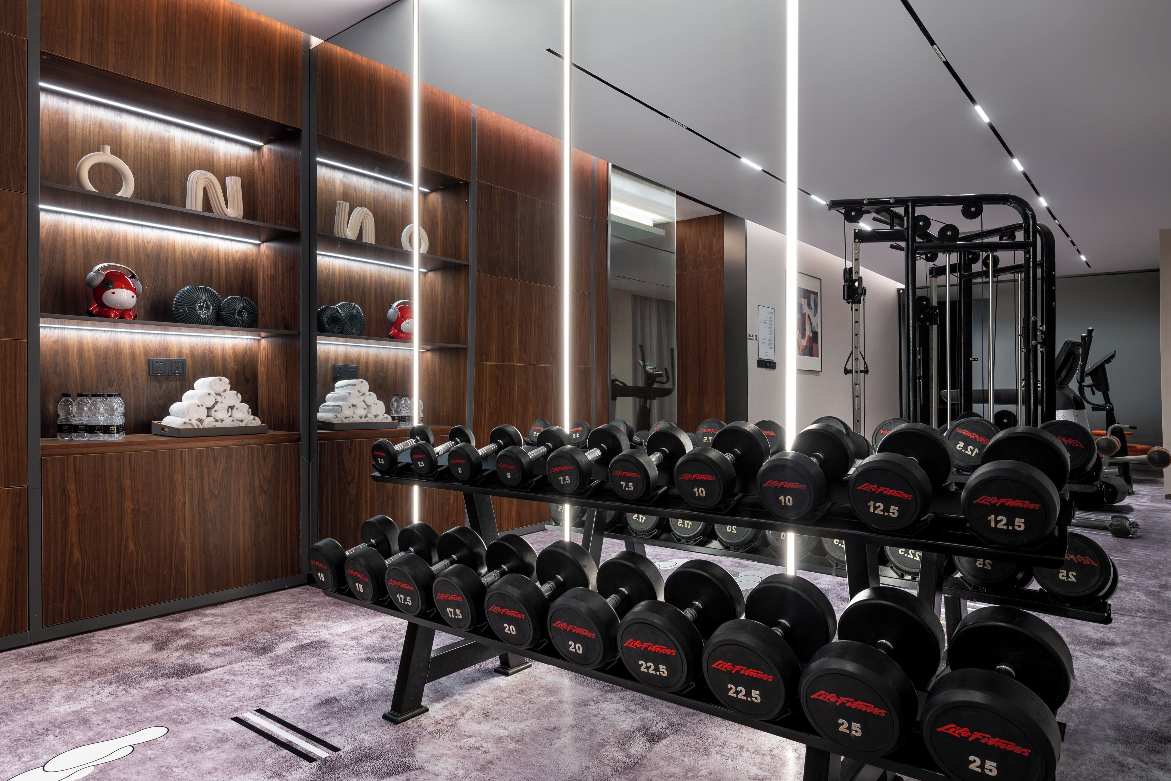 Un gimnasio con equipo de levantamiento de pesas, un espejo y estanterías de madera con diversos objetos.