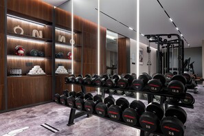 A gym with weightlifting equipment, a mirror, and wooden shelves with various items. - UrCove By Hyatt Yangzhou Dongguan Street (Yangzhou)