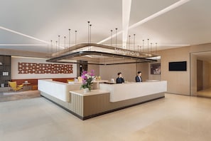 A modern reception desk with a glass partition, a seating area with a yellow chair, and a decorative wall with geometric patterns. - Keymore Residence Guangzhou (Guangzhou)