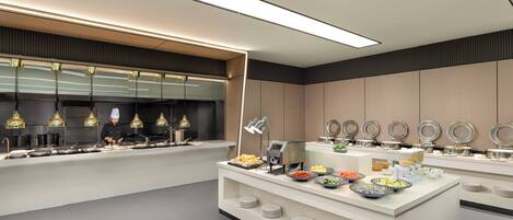 A modern buffet setup with a variety of food items and a chef preparing food.