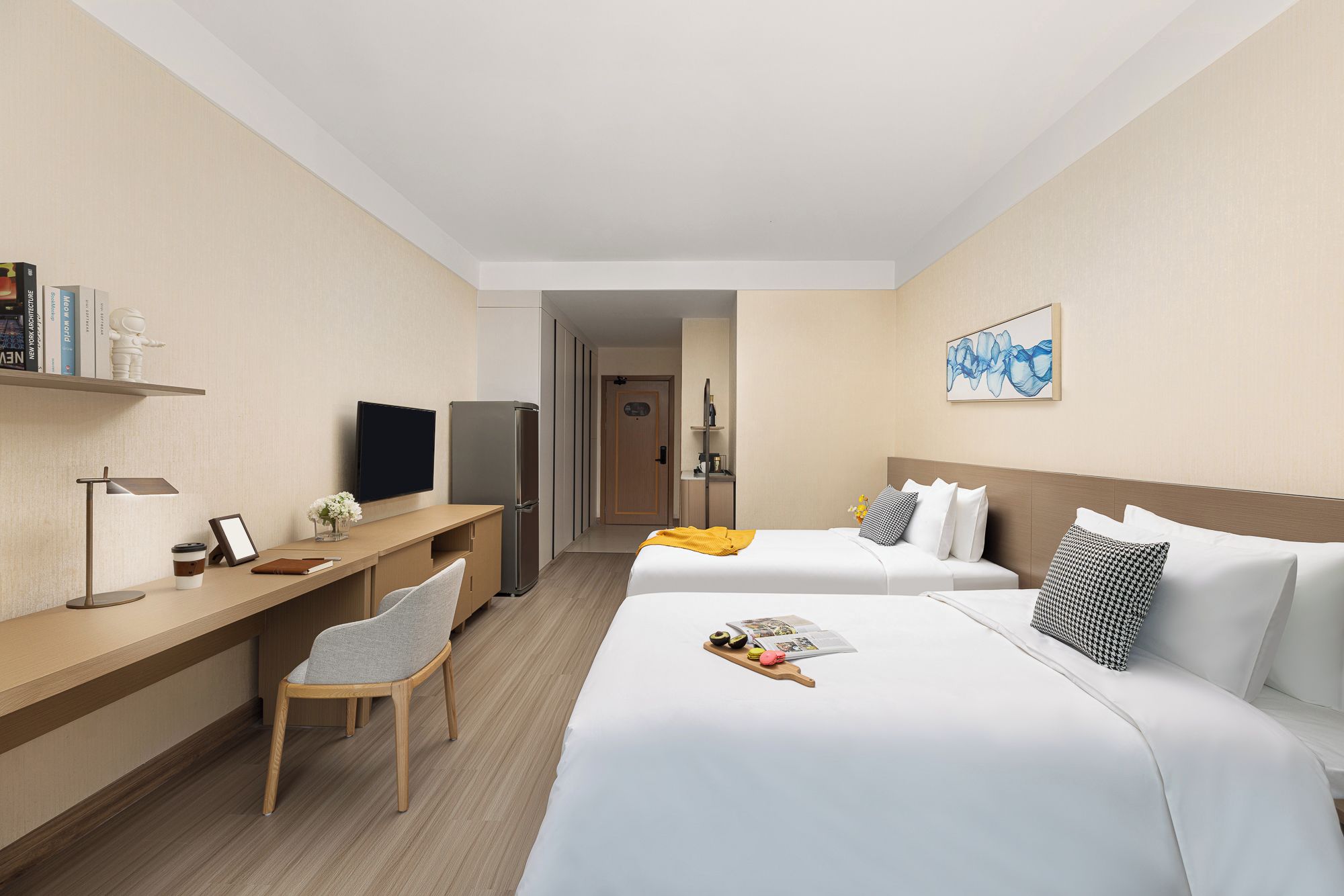 Ein Hotelzimmer mit Bett, Nachttisch, Stuhl, Schreibtisch, Fernseher, Kühlschrank und Wandbild.