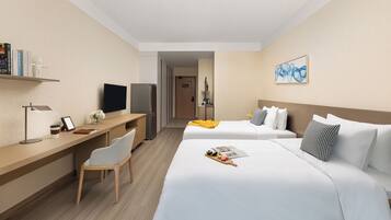 Ein Hotelzimmer mit Bett, Nachttisch, Stuhl, Schreibtisch, Fernseher, Kühlschrank und Wandbild.