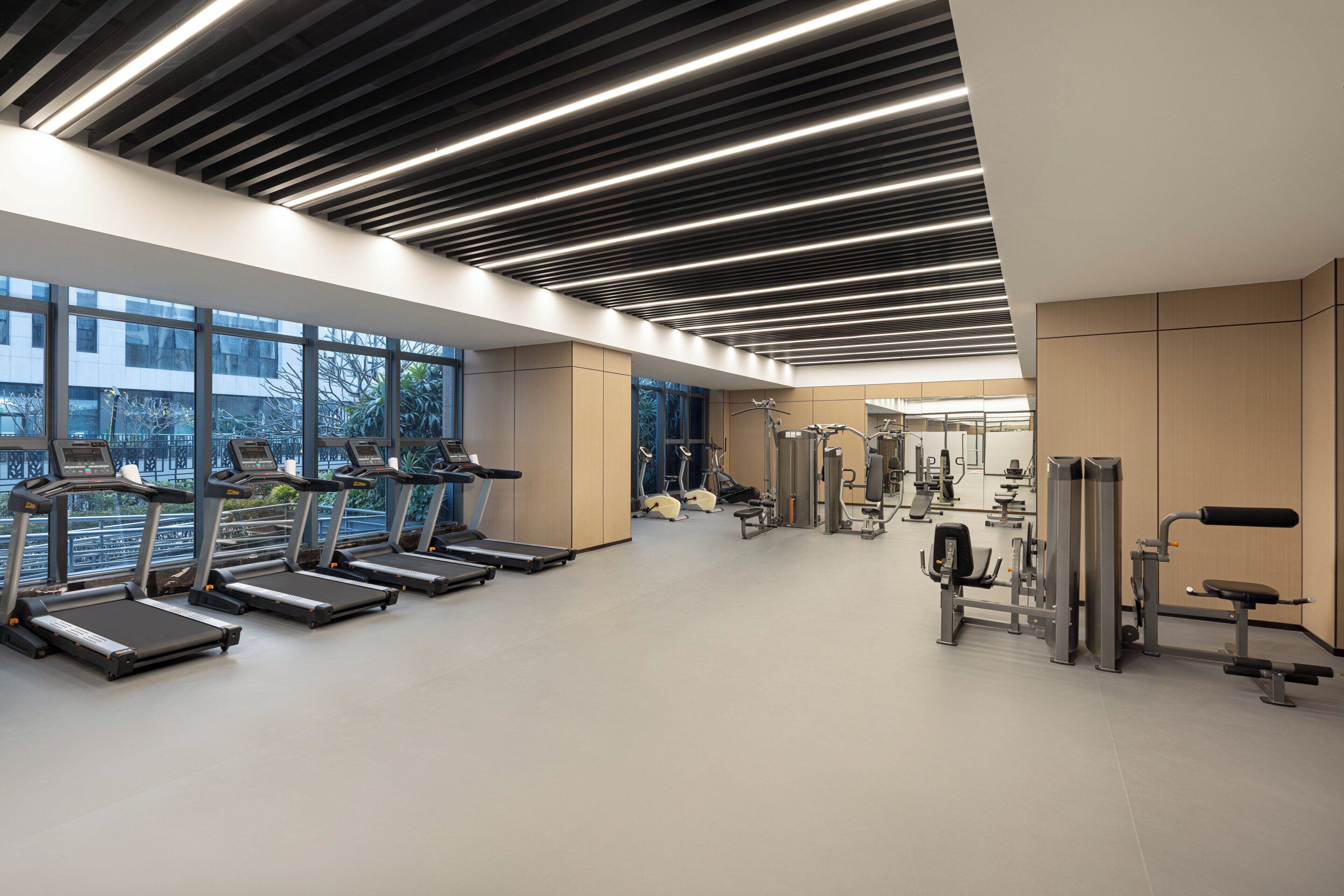 Un gimnasio moderno con cintas de correr, máquinas de pesas y un amplio ventanal con vistas al exterior.