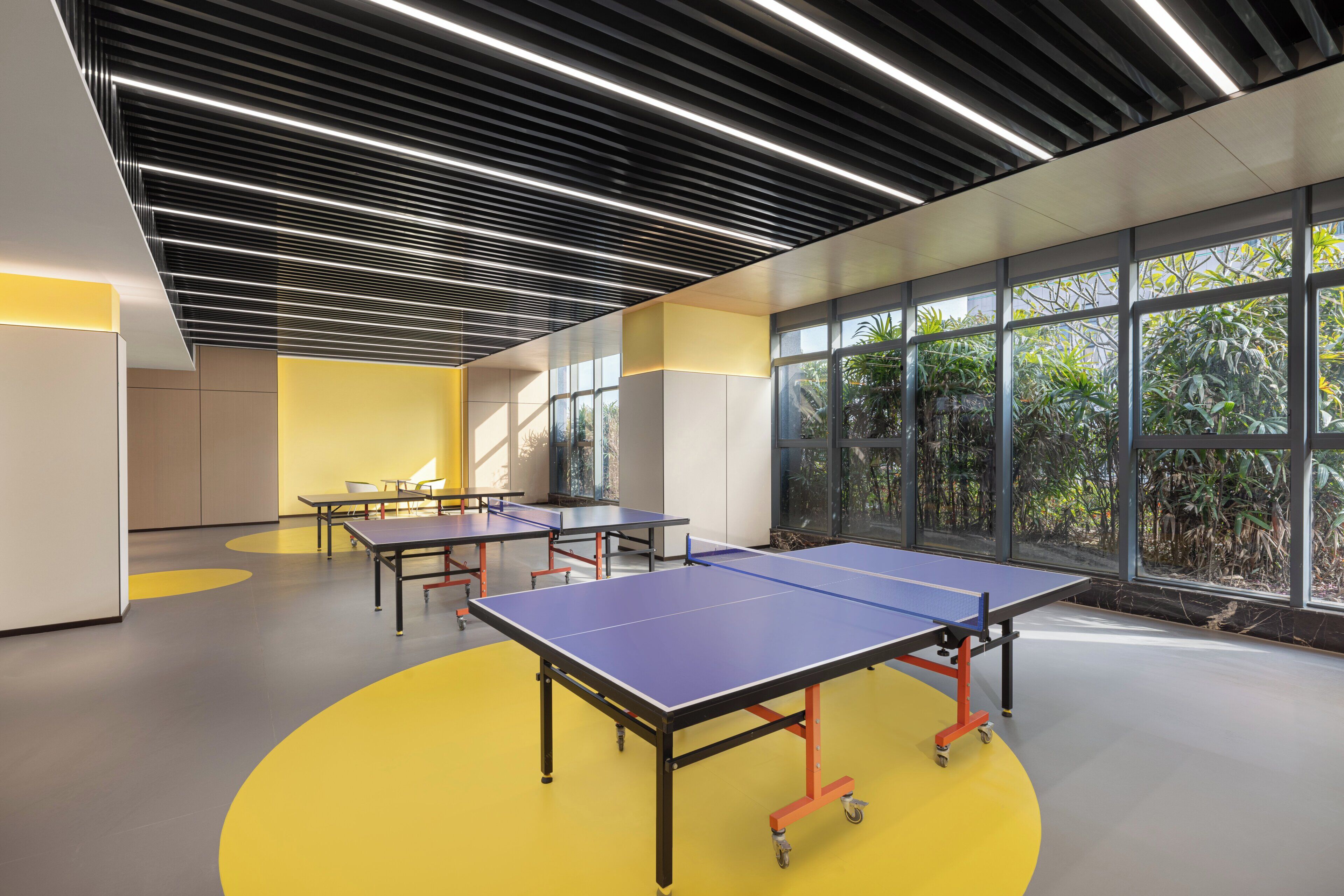 A modern indoor space with ping pong tables, large windows, and a yellow floor.