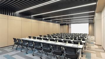 A conference room with rows of tables and chairs, a large screen at the front, and a patterned carpet.