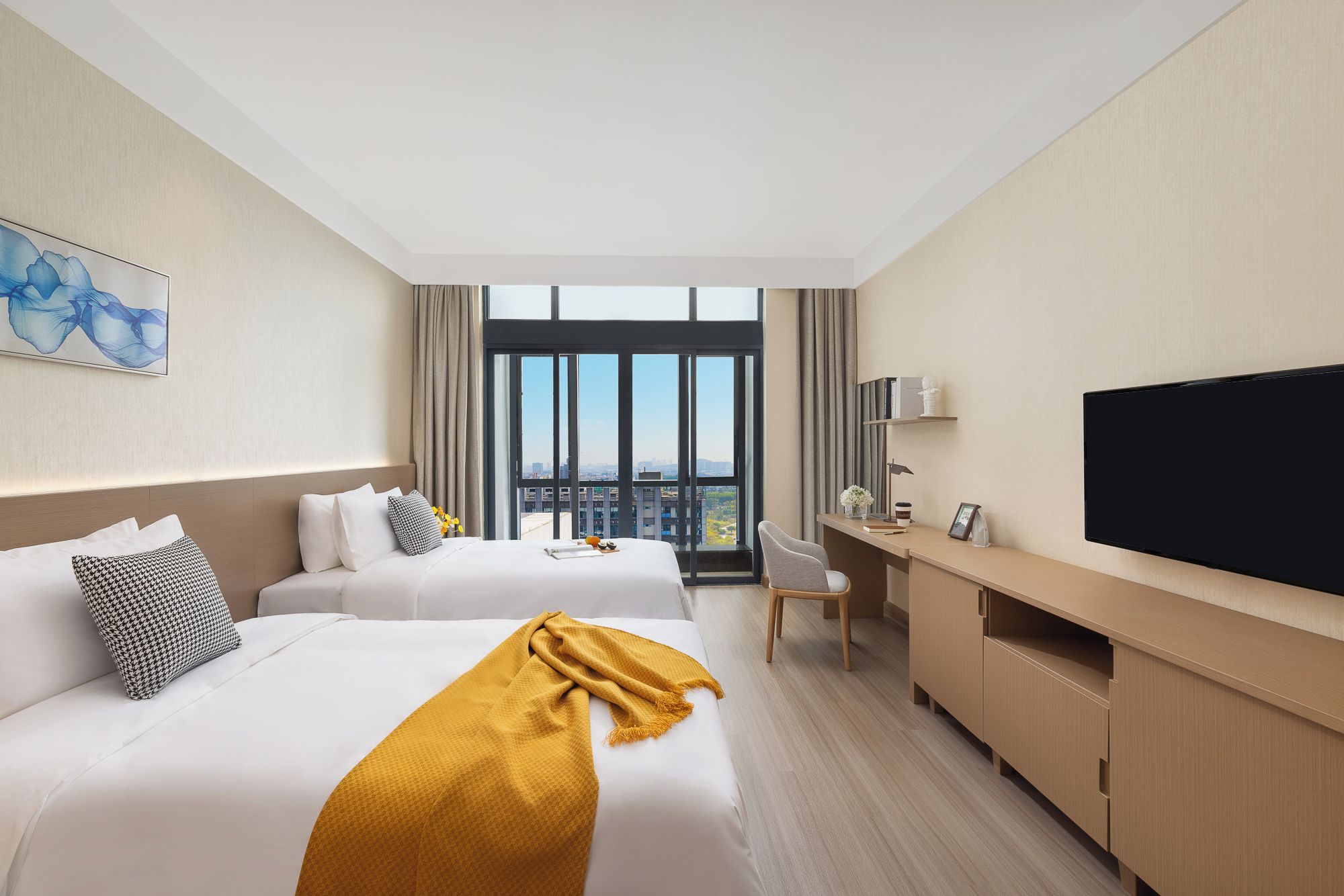 Ett hotellrum med två sängar, ett skrivbord, en tv och ett stort fönster med utsikt över staden.