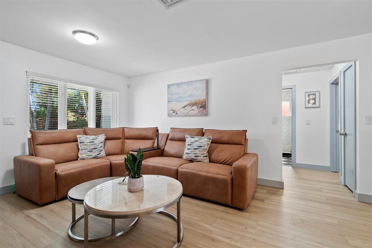 Een moderne woonkamer met een bruine leren bank, een ronde glazen salontafel en een schilderij aan de muur.