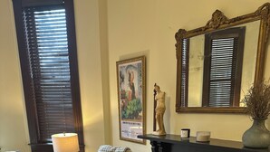 A living room with a sofa, armchair, and a small table with a lamp. There is a fireplace with a mirror above it and a framed picture on the wall.
