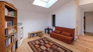 A spacious room with a skylight, a wooden bookshelf, a brown sofa, and a patterned rug.
