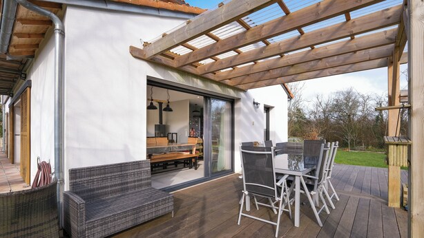 A covered outdoor patio with a dining table and chairs, a sofa, and a wooden pergola.