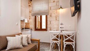 A cozy living area with a sofa, two chairs, a small table, a TV mounted on the wall, and a window with a curtain.