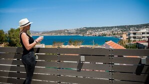 A woman standing on a bench overlooking a coastal town with a clear view of the sea and buildings.