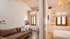 A cozy room with a sofa, a bed, a small table, and a chair. There are two windows with curtains.