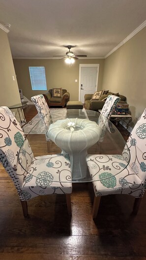 A dining area with a glass-top table surrounded by patterned chairs. - The Baker:  2-bedroom townhome. Walk to LSU (Baton Rouge)