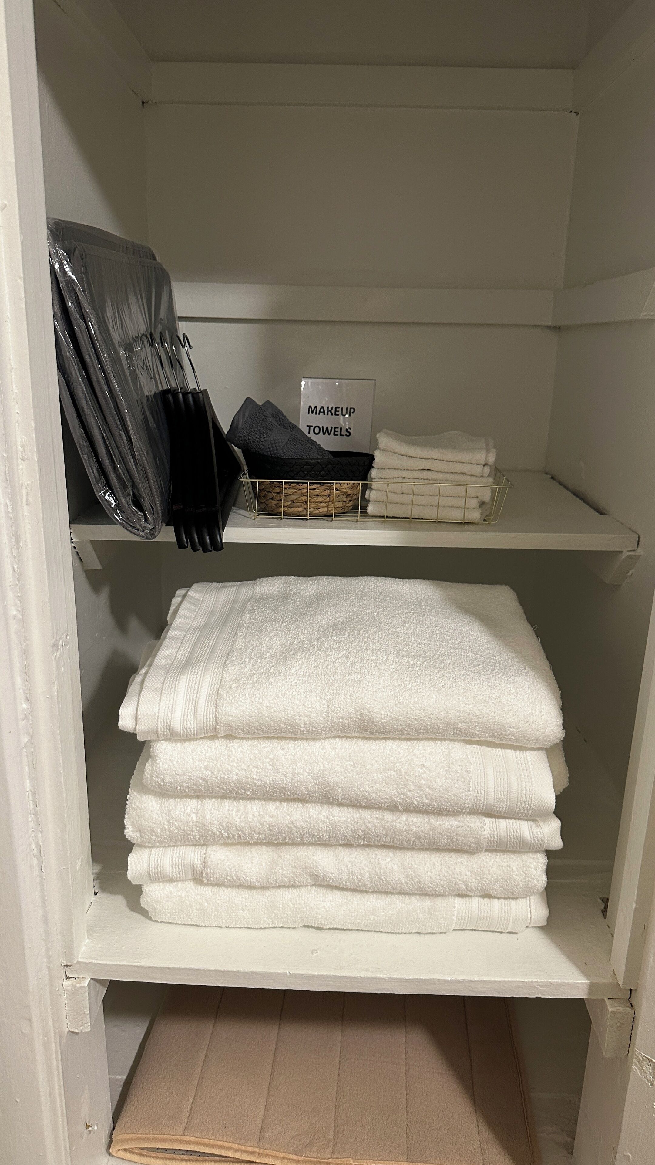 A storage area with shelves holding makeup towels, a basket, and a sign indicating the towels' purpose.