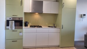 Cocina compacta con estufa a gas, horno y pileta, que presenta gabinetes verde claro y un salpicadero de azulejos.