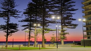Un paseo marítimo con farolas y altos árboles, con vistas al mar al anochecer.