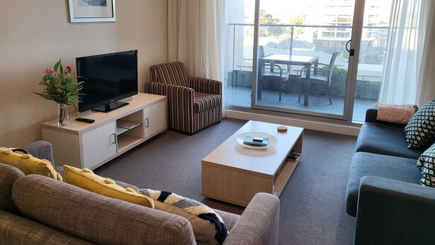 Una sala de estar moderna con un televisor de pantalla plana, un sillón a rayas, un sofá y un balcón con mobiliario exterior.