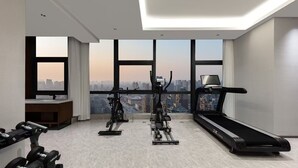 A modern gym with a treadmill, elliptical, and dumbbells, large windows with a city view, and a minimalist design. - UrCove by Hyatt Lianyungang Railway Station Suning Plaza (Lianyungang)