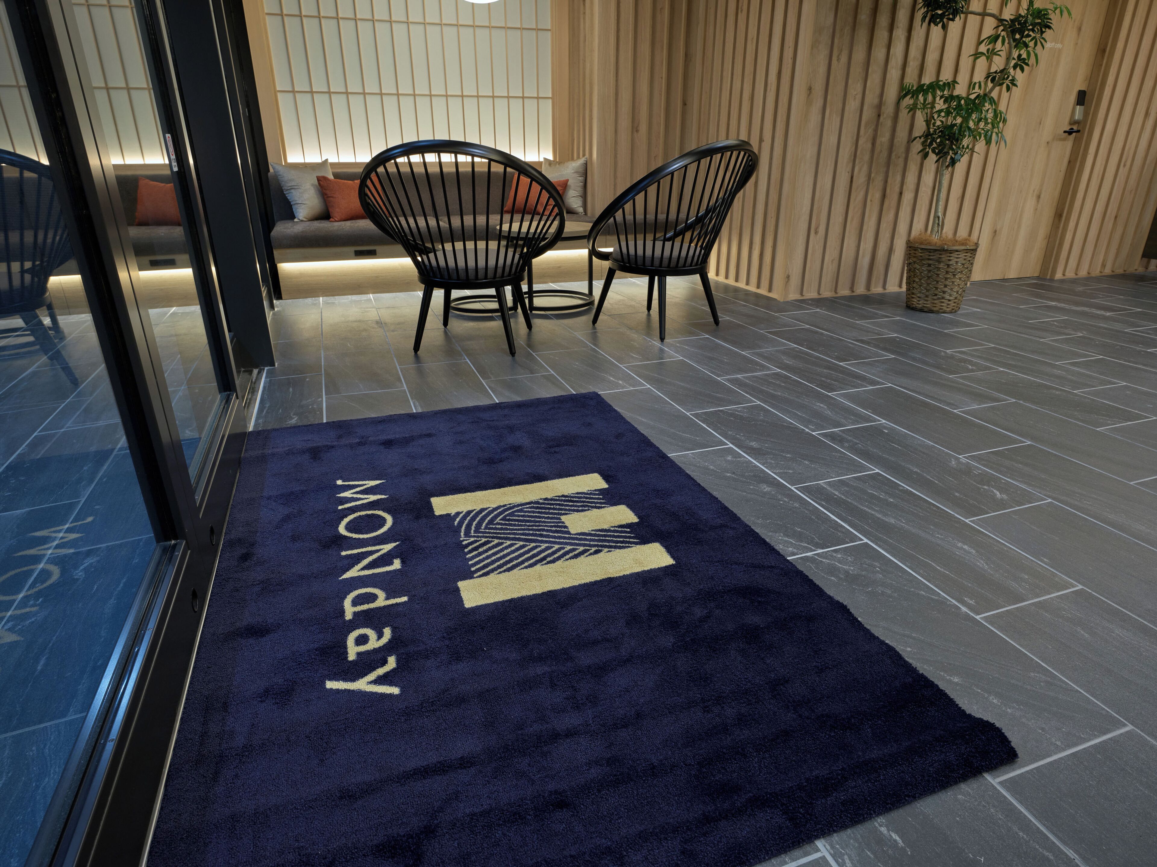 A reception area with a dark blue carpet, two black chairs, a wooden wall, and a potted plant.