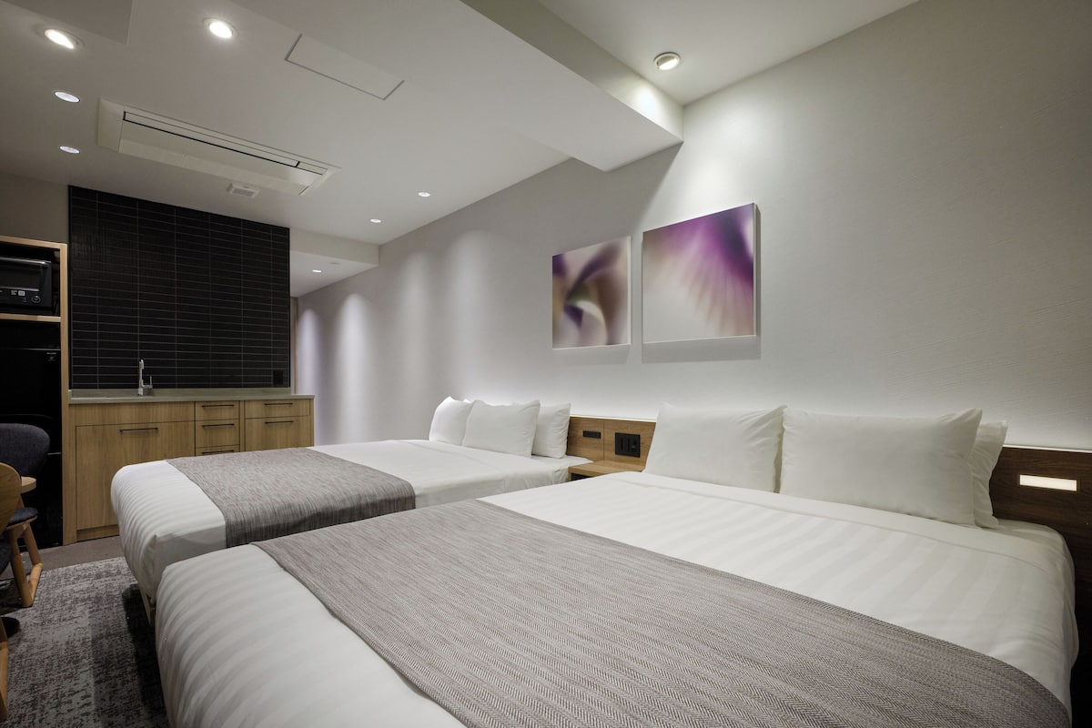 A hotel room with two beds, a desk, and a kitchenette.