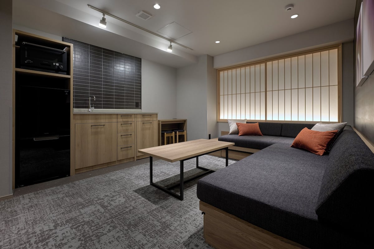 A compact living space with a kitchenette, a sofa, a small table, and a sliding shoji screen.