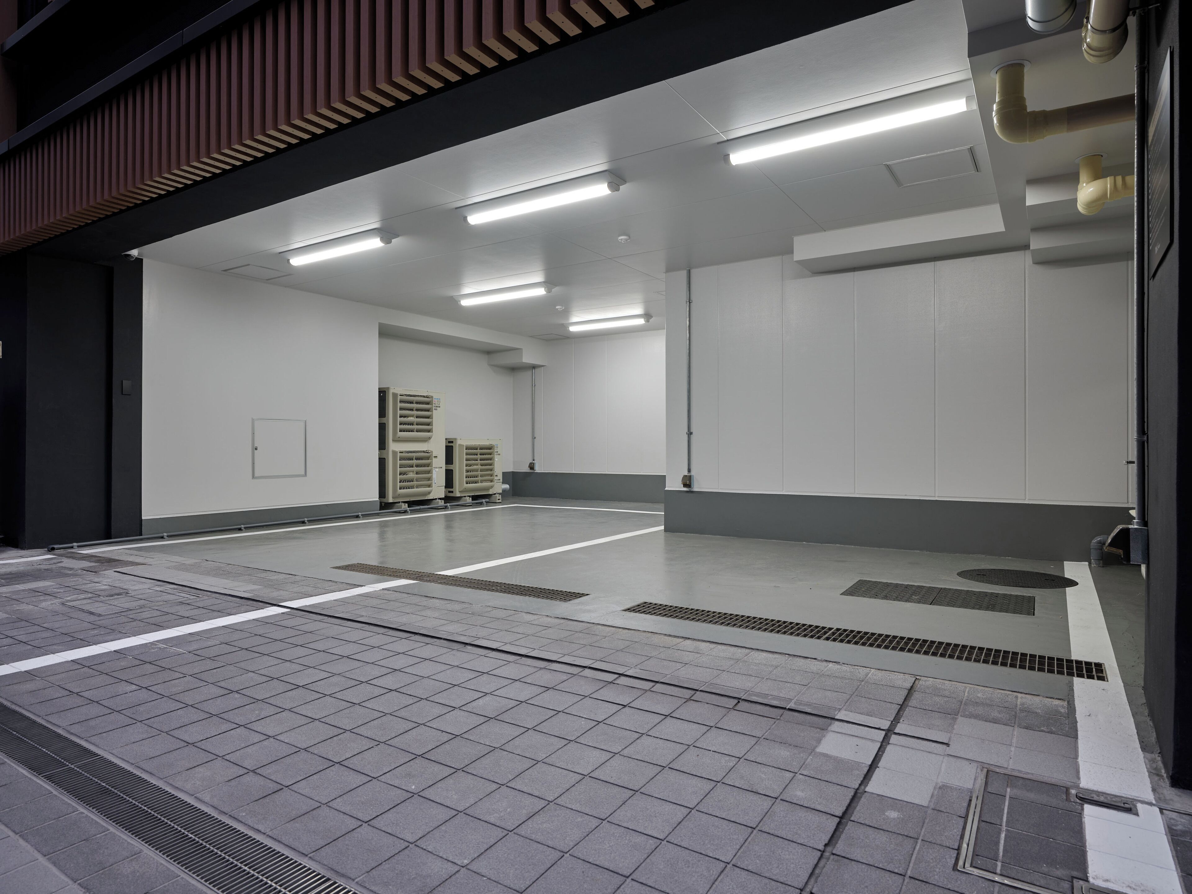 A spacious, well-lit indoor area with a tiled floor, ventilation ducts, and a large white wall.