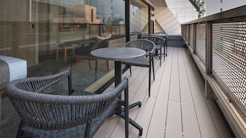 A balcony with wicker chairs and a round table, overlooking a cityscape.