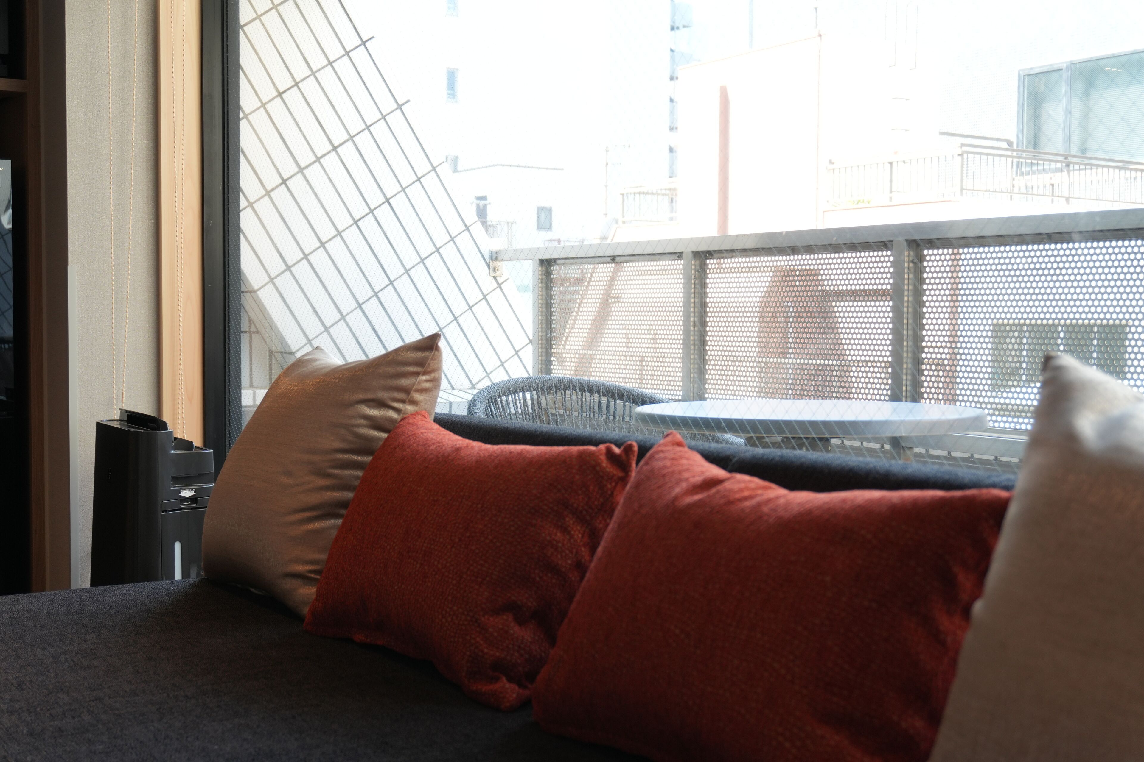 A room with a sofa, pillows, a small table, and a window with a view of buildings.
