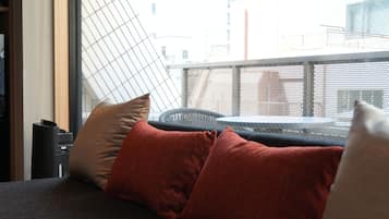 A room with a sofa, pillows, a small table, and a window with a view of buildings.