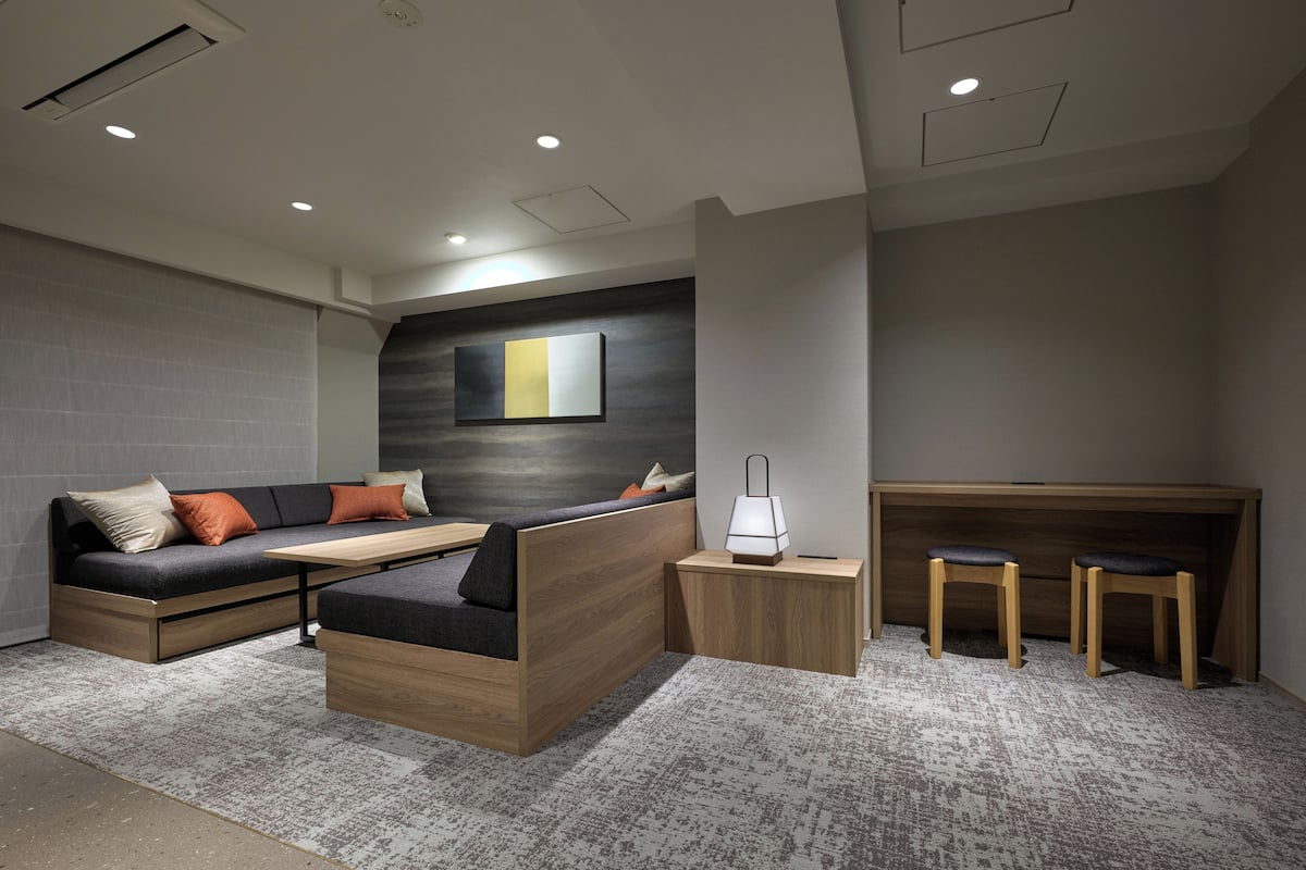 A modern living room with a sofa, a coffee table, a side table with a lamp, and a wooden desk with two chairs.
