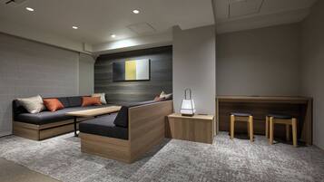 A modern living room with a sofa, a coffee table, a side table with a lamp, and a wooden desk with two chairs.