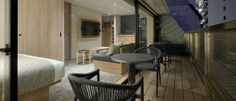 A modern hotel room with a balcony, furnished with a sofa, chairs, and a small table.