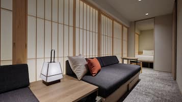 Una habitación moderna con sofá, una mesita de noche con lámpara y una cama al fondo.