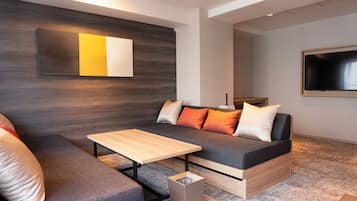 A modern living room with a grey sofa, wooden coffee table, and a small trash bin.