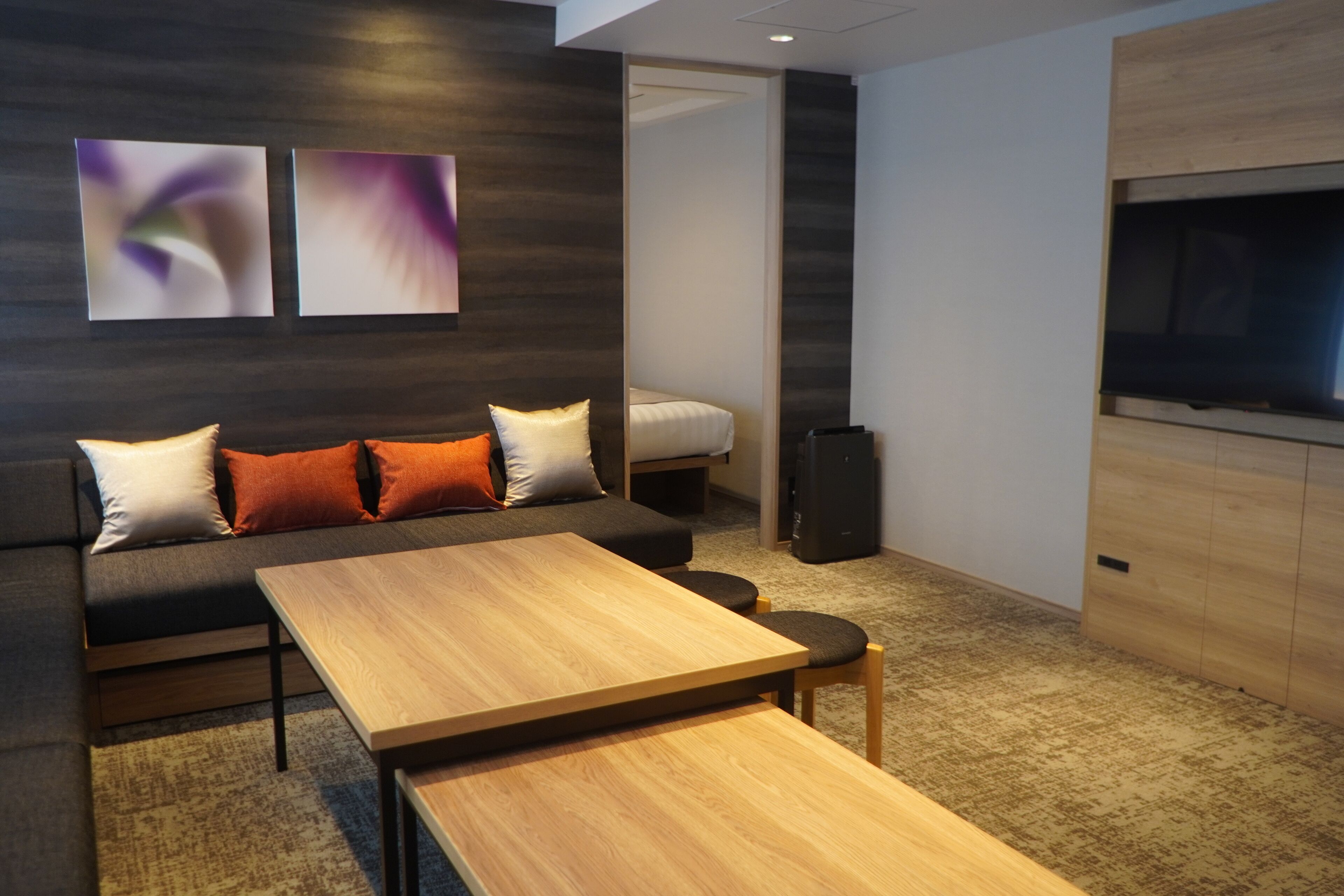 A modern hotel room with a sofa, a wooden table, a TV, and abstract wall art.